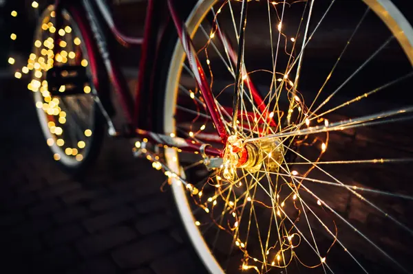 Close up a bicycle wheel with white Christmas lights wrapped around the spokes.