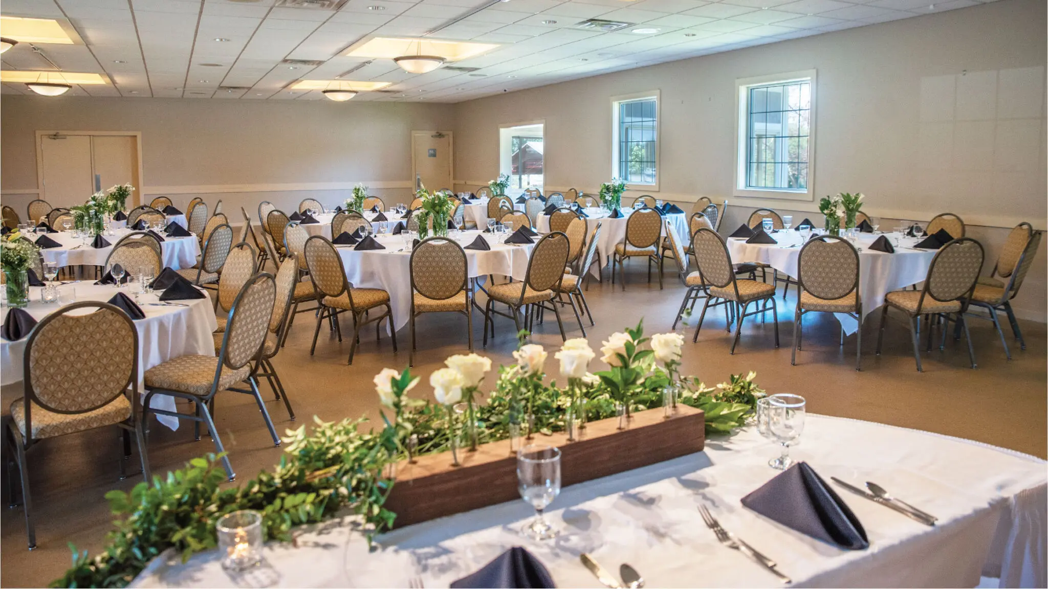 A intimate wedding reception in the Ingleside Pavilion with white tablecloths, navy blue accents, and white flowers.
