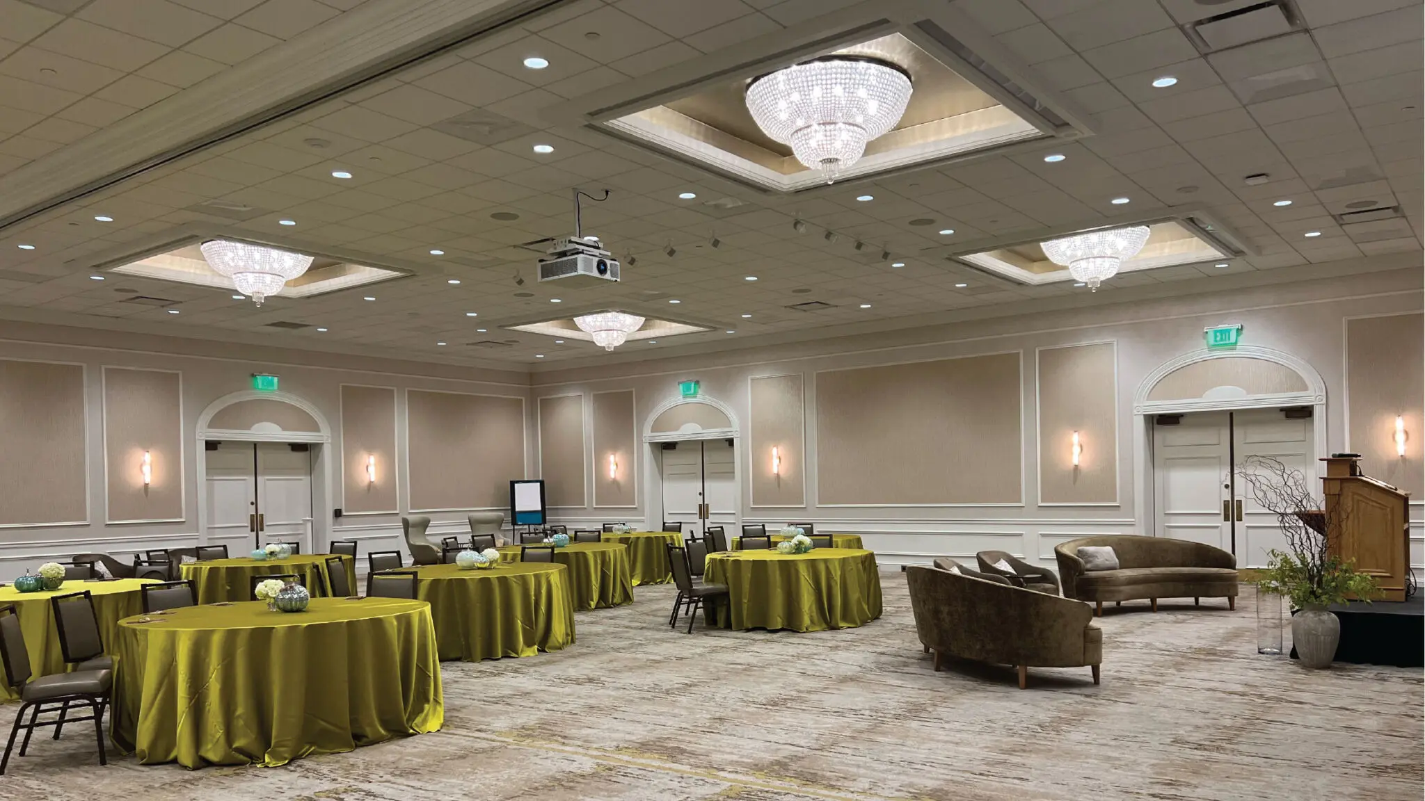 Oakton ballroom with green velvet round tablecloths, a stage, and soft seating.