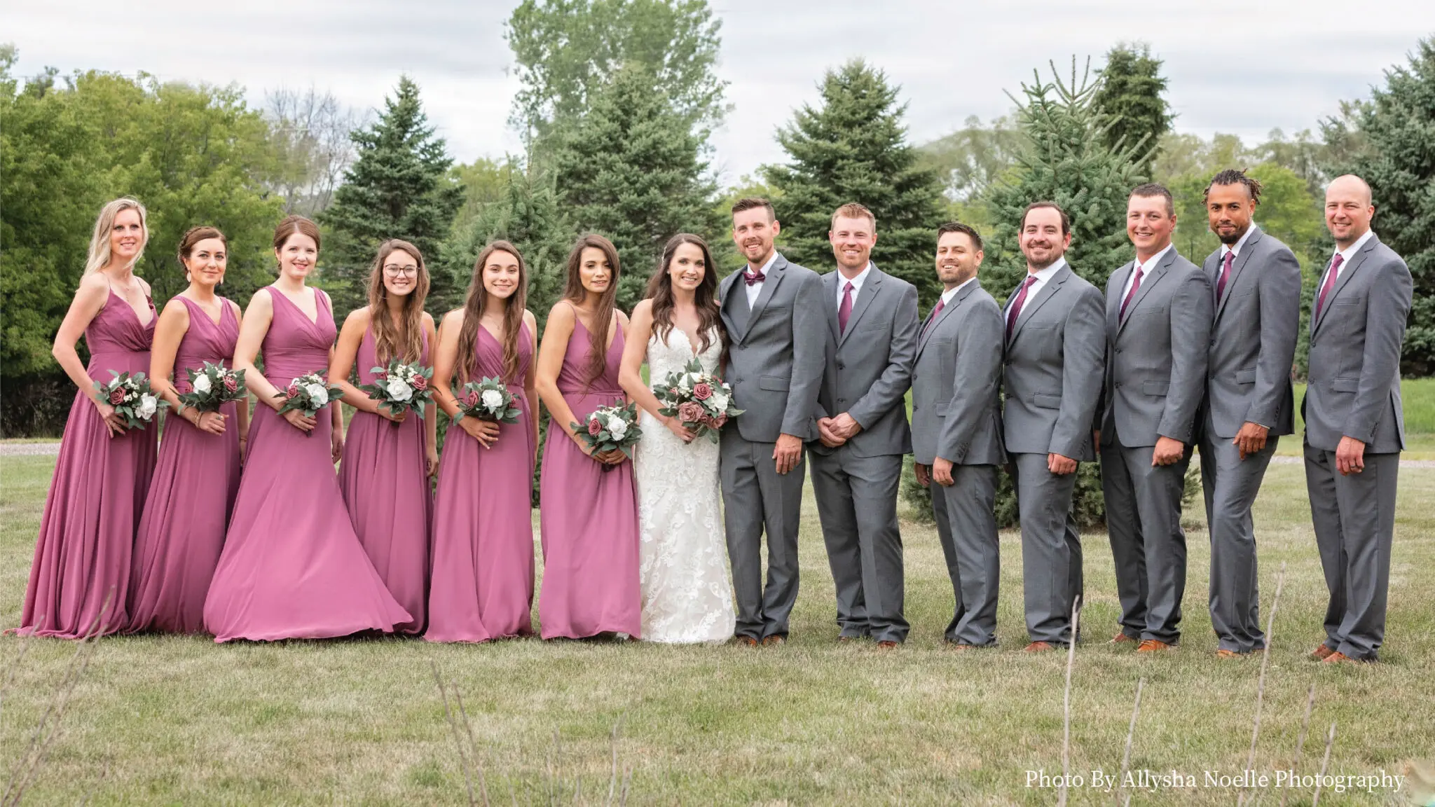 Wedding couple and party posing in a line outside in picturesque greenspace.