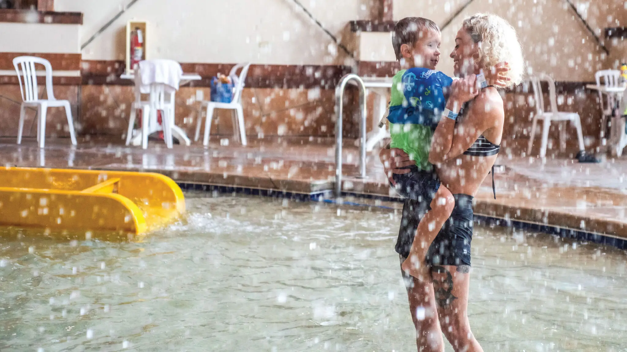 Mother holding her son under splashing water.
