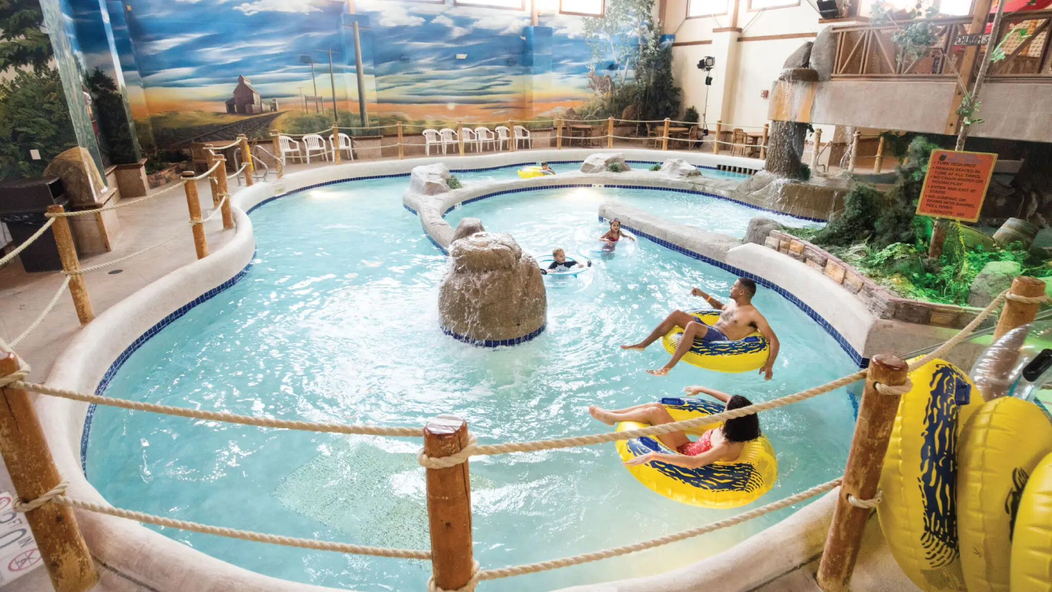 People floating on yellow tube on a winding lazy river in an indoor water park.