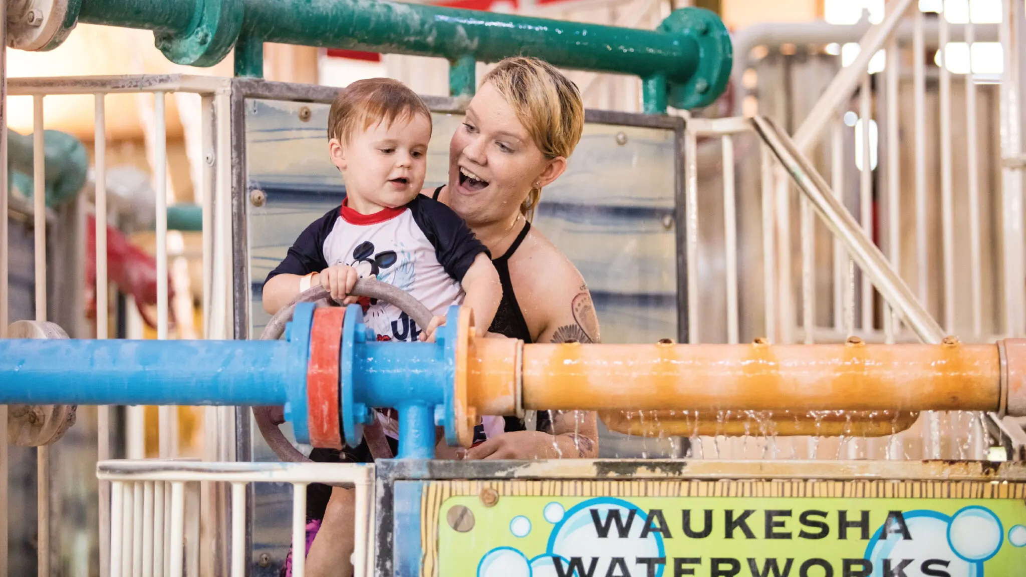 Mother holding her son to play with some water features in a water play structure.