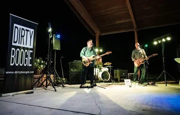 Band playing under the bandshell at night with stage lights.