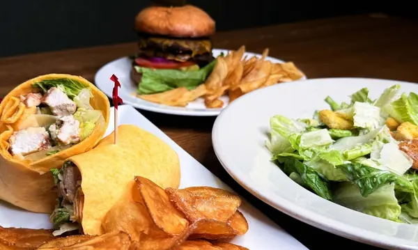 Caesar Wrap, Caesar Salad, and cheeseburger on wooden table.