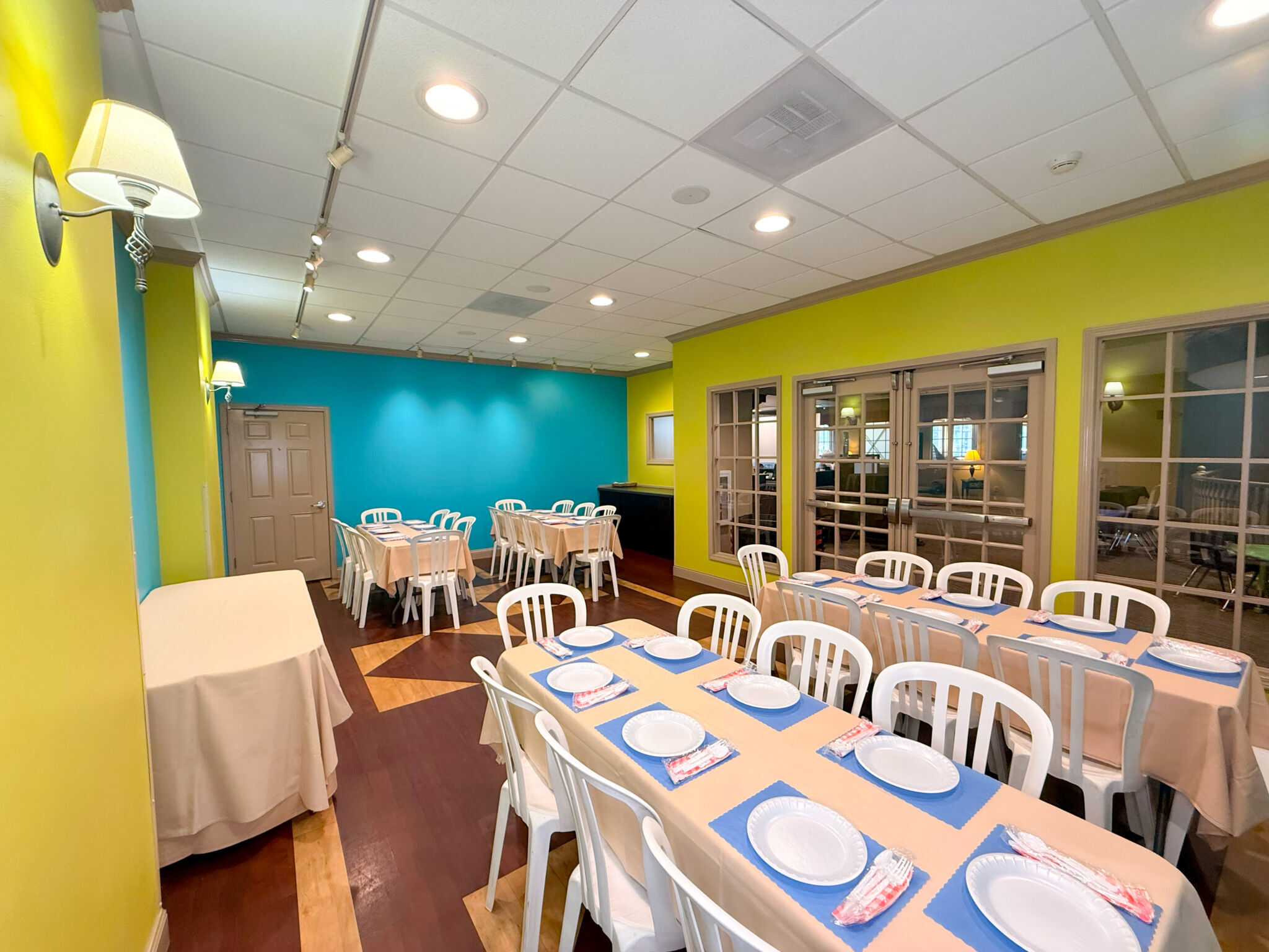 The teal and lime green upper party room with rectangular tables, cream tablecloths, and white chairs. 